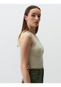 Enganliegendes, geripptes ärmelloses Top in hellem Beige mit rundem Ausschnitt. Kombiniert mit hochgeschnittenen, olivgrünen Hosen.