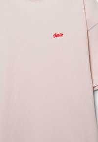 Chemisette rose clair avec petit logo rouge brodé sur le côté gauche de la poitrine portant l'inscription « Santa ».