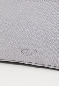 Borsa in tessuto grigia con superficie texturizzata e un logo sottile in grigio chiaro. Angoli arrotondati e dettagli di design minimalisti.