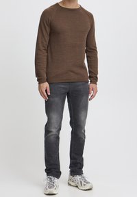 Brun långärmad tröja med rund hals, ribbade manschetter och strukturdetalj, kombinerad med grå slim-fit jeans och ljusa sportskor.