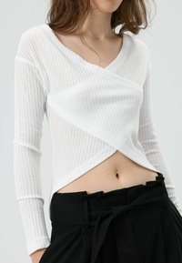 Wit geribd top met lange mouwen, omslagontwerp en V-hals, gecombineerd met hoogwaardige zwarte broek met ceintuurdetails.