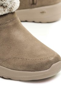Braune Wildleder-Ankle Boots mit einem Kunstfellkragen, runder Zehenform und einer cremefarbenen Gummisohle mit strukturierten Grip-Mustern.