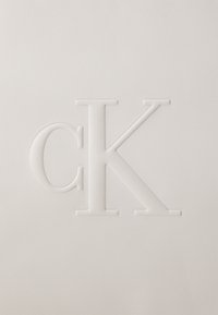Superficie bianca testurizzata con un logo in rilievo che presenta una 'c' minuscola e una 'K' maiuscola in un carattere semplice e moderno.