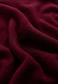 Burgundská vlněná tkanina s jemným, strukturovaným povrchem, vykazující jemné záhyby a variace na povrchu. Bohatá, hluboká barva s jemným leskem.