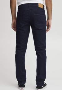 Jeans de mezclilla azul marino con corte ajustado, que cuentan con dos bolsillos traseros, una etiqueta de cuero sobre el bolsillo derecho y un diseño de pierna recta.