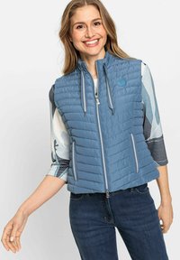 Blauer isolierter Weste mit horizontalem Steppmuster, Front-Reißverschluss, zwei Seitentaschen und kontrastierender grauer Abrundung. Kombiniert mit einem gemusterten Oberteil.