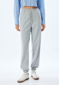 Lichtgrijze joggingsbroek van een zacht materiaal met een elastische tailleband en boorden. Gecombineerd met witte sneakers met een beige zool.