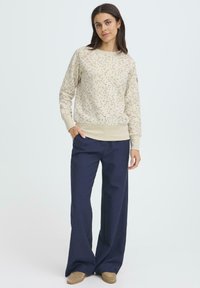 Svetlo béžová mikina s farebnou kvetinovou potlačou, rebrovanými manžetami a lemom. Kombinovaná s námorníckymi širokými nohavicami a hnedými mokasínami na nosenie bez šnúrok.