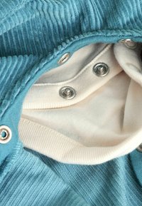 Blaues Cordstoffgewebe mit vertikalen Rillen, ausgestattet mit metallenen Druckknöpfen und einem weichen beigen Innenfutter. Glatte Textur und kontrastierende Farben.