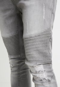 Pantalones de denim gris con acentos acanalados en las rodillas, detalles desgastados y un diseño de ajuste slim. Sin hardware visible ni patrones adicionales.