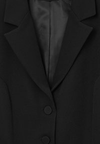 Blazer nero con colletto strutturato, due grandi bottoni rotondi e una fodera in satin morbido. Il tessuto presenta una trama sottile.