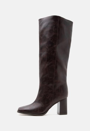 Botte en cuir marron foncé montant jusqu'au genou avec talon bloc et bout pointu, présentée sur un fond clair uni.