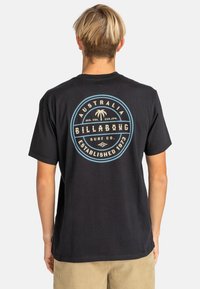 Black cotton T-shirt featuring a circular graphic with "Billabong Surf Co." and a palm tree design, accented with blue and cream colors.