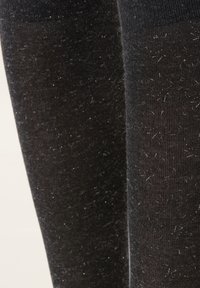 Chaussettes noires montant jusqu'au genou avec une surface texturée, présentant un mélange de fibres opaques et légèrement brillantes, et une apparence douce et duveteuse.