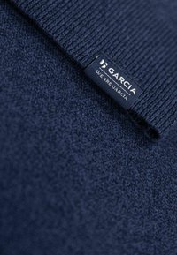 Marineblauwe trui met een geribbelde kraag, zachte textuur en een label met het merk "Garcia" en de slogan "WE ARE GARCIA."