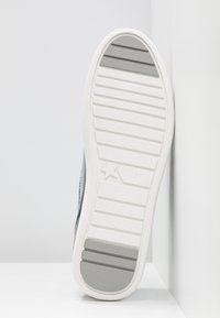 Semelle blanche avec grip texturé, comportant une section gris clair et un détail étoile. La base de la chaussure est inclinée sur un fond neutre.