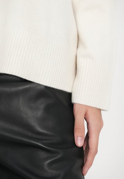 Cream-colored sweater with ribbed hem and cuffs, paired with a black leather skirt, showcasing smooth texture and layered design.