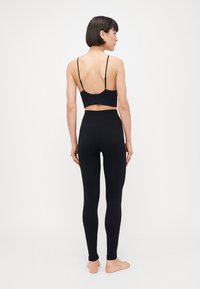 Sort sportsbh med tynne stropper og utskåret rygg, kombinert med høyt liv svarte tights, begge laget av glatt, elastisk stoff.