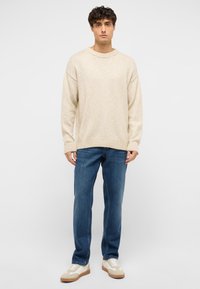 Pull en maille beige avec un col et des poignets côtelés, associé à un jean en denim bleu et des baskets crème avec des accents marron.