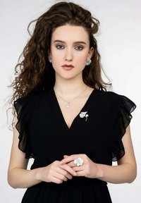 Vestido negro con mangas acampanadas. Los accesorios incluyen pendientes florales de plata, un colgante y un anillo con un diseño de flor texturizada.