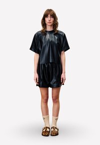 Zwart nepleer oversized top en korte broek met een gladde textuur. Draag deze met beige sokken en slip-on schoenen met luipaardprint.