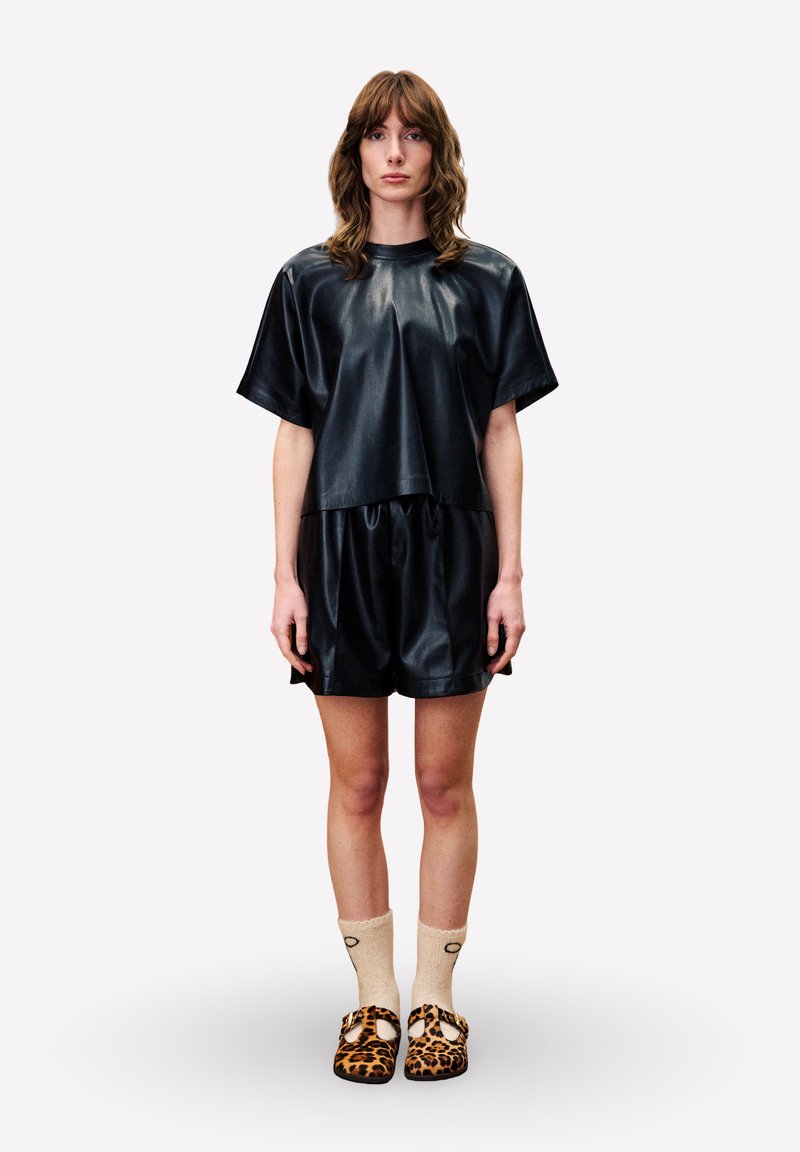 Zwart nepleer oversized top en korte broek met een gladde textuur. Draag deze met beige sokken en slip-on schoenen met luipaardprint.