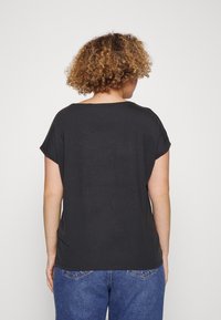 Czarny t-shirt z krótkim rękawem o luźnym kroju, z okrągłym dekoltem i gładką fakturą, zestawiony ze spodniami dżinsowymi w średnim odcieniu.
