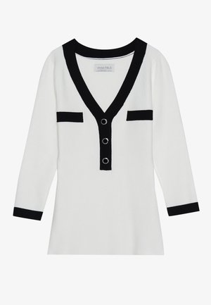 Hvit cardigan med svarte detaljer, V-hals, tre store knapper og to frontlommer, har lange ermer og en myk tekstur.