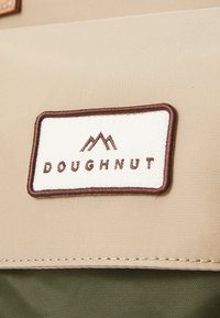 Tan fabric patch with "DOUGHNUT" text and mountain graphic in dark brown embroidery, set against a green background texture.