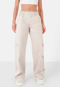 Beige cargobroek met een elastische tailleband, rechte pijpen en meerdere zijzakken, voorzien van een vlakke voorkant en subtiele stikseldetails.