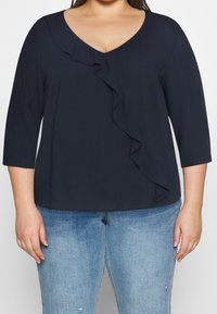 Top blu navy con maniche a 3/4, scollo a V e dettaglio arricciato sulla parte anteriore. Realizzato in un tessuto morbido con un fit rilassato, abbinato a jeans azzurri.
