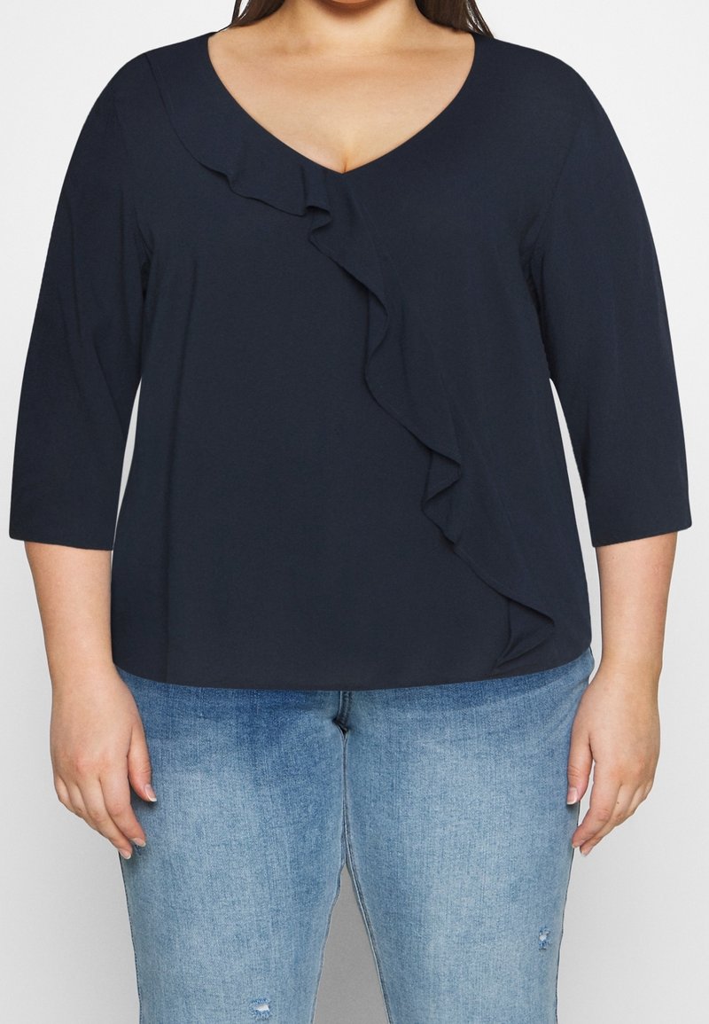 Top blu navy con maniche a 3/4, scollo a V e dettaglio arricciato sulla parte anteriore. Realizzato in un tessuto morbido con un fit rilassato, abbinato a jeans azzurri.