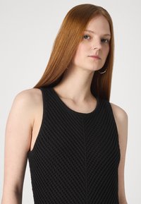 Top sem mangas preto com um design de malha texturizada em padrão de diamante e decote redondo. Tecido suave e silhueta ajustada.