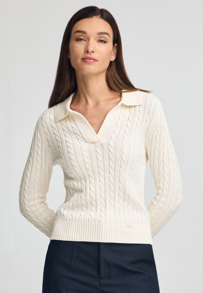 Strickpullover in Off-White mit Zopfmuster, V-Ausschnitt und geripptem Saum. Verfügt über eine weiche Textur und lange Ärmel.
