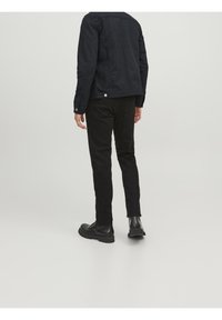 Svart denimjacka med krage, långa ärmar och tryckknappar, som bärs med svarta tajta byxor och kraftiga svarta stövlar, allt mot en neutral bakgrund.