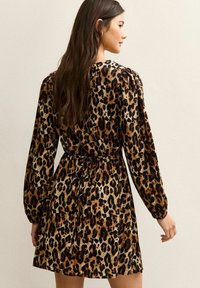 Robe à imprimé léopard avec de longues manches bouffantes, taille cintrée et coupe décontractée. Le tissu présente une texture brillante avec des tons marron, noir et beige.