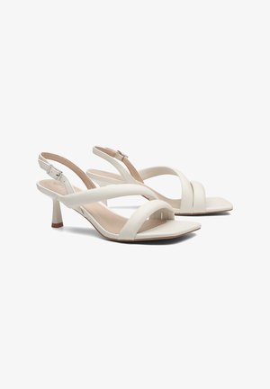 Sandales slingback blanches pour femme avec bout carré, deux larges brides, boucle réglable et petit talon kitten sur fond blanc.