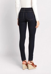 Donkerblauwe skinny jeans met contrasterende oranje stiksels, hoge tailleband, twee achterzakken, gecombineerd met bruine wedge sandalen.