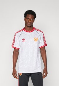 Witte korte mouwen shirt met rode accenten, voorzien van geometrische patronen, Adidas-logo en Manchester United-embleem op de linkerborst.