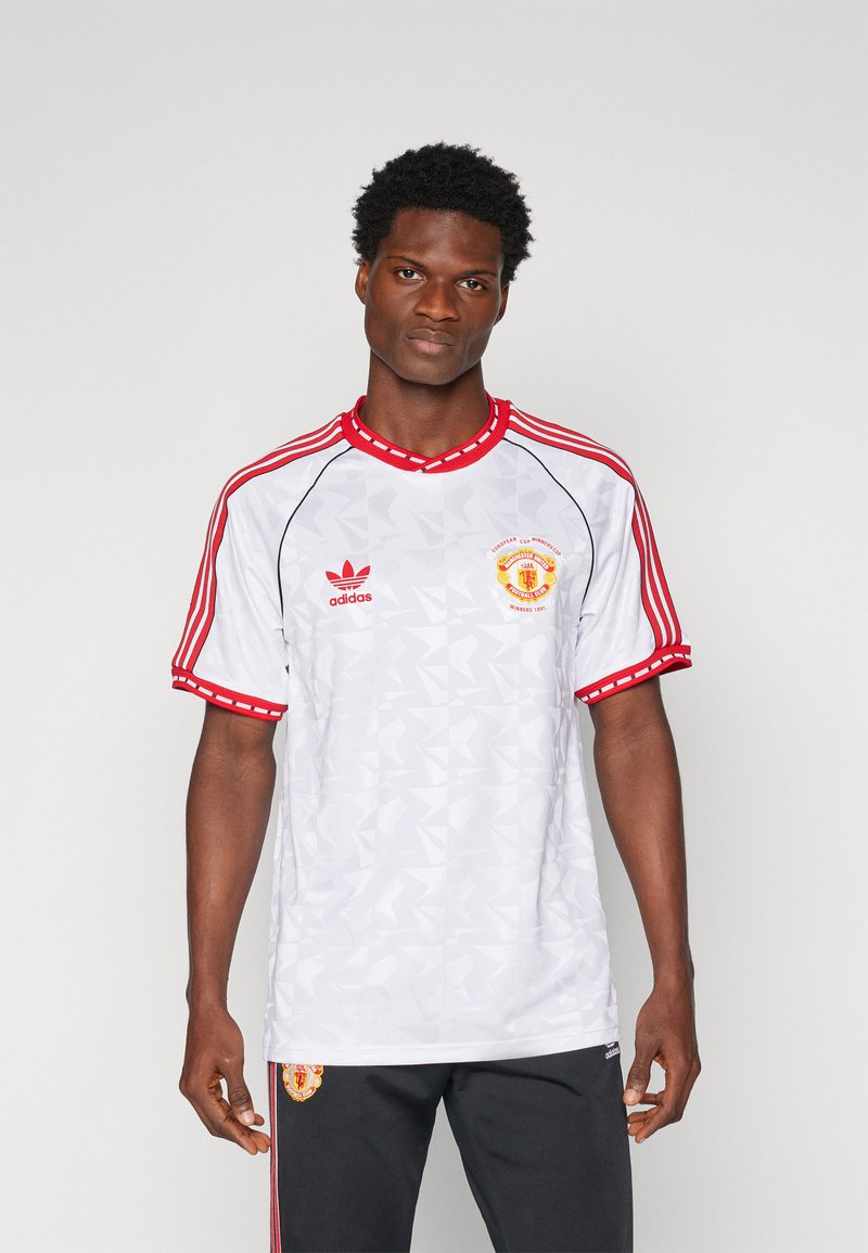 Witte korte mouwen shirt met rode accenten, voorzien van geometrische patronen, Adidas-logo en Manchester United-embleem op de linkerborst.