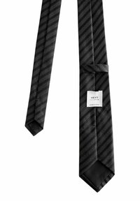 Nœud papillon noir avec des rayures diagonales et de petits motifs en pointillés. Texture satinée, extrémités effilées, et une étiquette indiquant "NEXT Tailoring, Fabriqué en Chine."