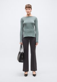 Fazonra szabott, hosszú ujjú, világoszöld felső hajónyak kivágással, sötétszürke, bővülő szárú nadrággal párosítva. A modell fekete kézitáskát tart, fekete cipőt visel.