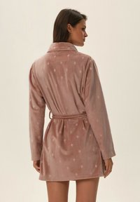 Duszony różowy, krótki, pluszowy szlafrok z paskiem w talii, długimi rękawami i wzorem w diamenty; miękka tekstura i kołnierzowy fason.