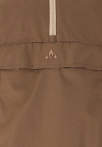 Ruskea kangas lähikuvassa, jossa on beige vetoketju ja pieni kirjailtu logo, joka esittää yhtä liekinmuotoa ja kahta kolmiota sen alapuolella.