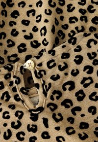 Bežs audums ar melniem leopardu plankumiem, ar pogu aizdari un mīkstu tekstūru. Raksts ir izteiksmīgs un vienmērīgi izvietots visā materiālā.