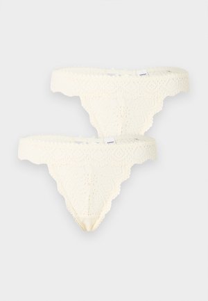 Două chiloți tip tanga din dantelă crem, cu margini ondulate și modele florale, fiecare cu o mică etichetă albă a brandului pe talie.
