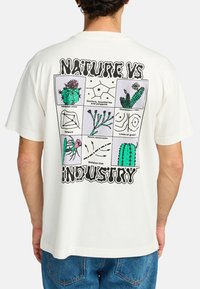 Cream short-sleeve t-shirt featuring a graphic print on the back with cacti, diagrams, and text "NATURE VS INDUSTRY" in black.