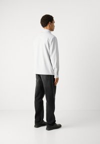 Cămașă albă cu mâneci lungi și guler, asociată cu pantaloni din denim negri. Costumul are un croi lejer și un design minimalistic.