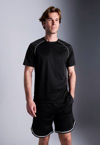 Conjunto atlético preto com camisa de manga curta e calções. O material parece liso; a camisa tem acabamento branco ao longo dos ombros e decote.