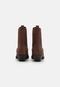 Braune Wildleder-Ankle-Boots mit niedrigem Absatz, ausgestattet mit elastischen Seitenpaneelen und Nähdetails. Die Rückansicht zeigt Zuglaschen.